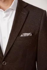Blazer de corte slim fit en color marrón con textura jaspeada, cierre frontal de dos botones, solapas clásicas y bolsillo en el pecho con pañuelo decorativo.