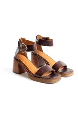 Sandalias de cuero color marrón oscuro, con diseño de punta cuadrada, taco ancho efecto madera, tira ancha en el empeine y talonera con tira al tobillo ajustable mediante hebilla metálica circular.