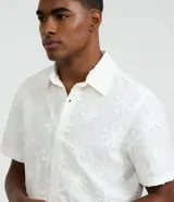 Camisa de manga corta color blanco con diseño bordado de flores, cuello inglés y cierre frontal de botones.
