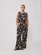 Pantalon de corte recto y holgado, confeccionado en algodón estampado con motivos playeros como palmeras, soles y caracoles en color crema sobre fondo negro. Posee cintura elástica.