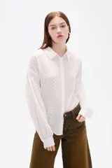 Camisa de color blanco con textura de pequeños puntos en relieve, cuello clásico, cierre frontal con botones y mangas largas con detalle de punto smock y puños elásticos.