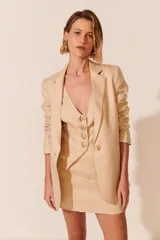 Blazer color beige de corte clásico, con solapas de muesca, cierre frontal con un botón dorado y bolsillos delanteros con solapa.