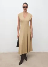 Vestido midi de manga corta en color beige, con cuello en V, diseño evasé, costuras decorativas visibles y cierre de cremallera en la parte posterior.