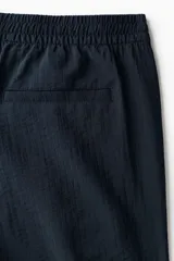 Pantalon corto de corte relajado color azul marino, confeccionado en tejido texturizado suave de mezcla de viscosa. Cuenta con cierre decorativo, cintura con elástico revestido y cordón de ajuste, bolsillos laterales discretos y bolsillo trasero insertado.