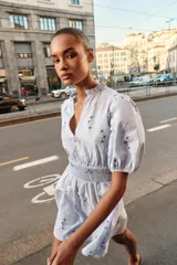 Vestido corto de color celeste con estampado floral, cuello redondo con volante y escote en pico. Presenta mangas cortas abullonadas con puños elásticos y cintura con nido de abeja elástico.