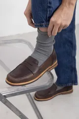 Mocasín de cuero vacuno en color marrón, con diseño bitono que combina texturas lisas y con grabado tipo cocodrilo en el empeine. Cuenta con detalle de estribo clásico y suela plana con vira en contraste.