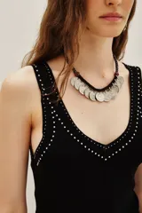 Musculosa negra de tejido de punto, ajustada al cuerpo, con escote en V y detalles de pequeños apliques blancos (similares a tachas o puntos) bordeando el escote y la cintura.