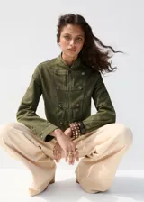 Chaqueta estilo militar color verde militar, confeccionada en algodón, con cuello alto, cierre frontal de cremallera y doble botonadura metálica decorativa.