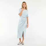 Vestido midi de color celeste, confeccionado en tejido de punto, con cuello redondo, mangas cortas y detalle de nudo o torsión en la cintura que genera un efecto drapeado, con una abertura frontal en la falda.