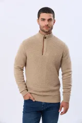 Buzo de punto color beige, con cuello alto y cierre frontal con cremallera y solapa de gamuza con botón. Presenta un tejido texturizado en el cuerpo y mangas lisas.