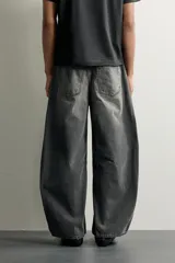 Jeans de denim de algodón color gris con efecto lavado, de corte relaxed barrel fit y tiro medio. Presenta diseño amplio con pinzas en las rodillas y costuras curvas, cierre frontal con botones y cinco bolsillos tradicionales.