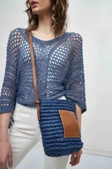 Bolso bandolera azul tejido con bolsillo de cuero marrón en el frente y correa larga de cuero marrón.