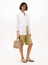 Cartera tote color beige con diseño calado del monograma TH en relieve. Tiene doble asa corta y correa larga extraíble. Incluye cierre magnético y detalles metálicos dorados.