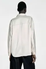 Camisa de manga larga confeccionada en tejido satinado, con cuello solapa, cierre frontal con botones y bajo asimétrico.