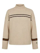 Polera de lana lambswool color beige, con cuello media polera y diseño de rayas horizontales en contraste en la parte superior delantera y en los puños. Presenta un corte amplio y largo a la cadera, con un pin metálico con el logo de la marca en la manga.