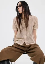 Cardigan de punto calado color beige, de diseño recto, cuello redondo, manga corta y cierre frontal con botones.