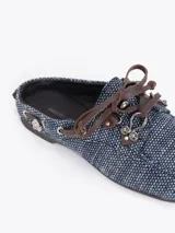 Zapato destalonado tipo slide color azul con diseño de micromotivo geomético, combinado con detalles de cordones y apliques de cuero marrón, ojales metálicos y un pasador metálico decorativo en el lateral.