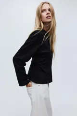 Top de manga larga en punto de algodón con cuello redondo, hombros caídos y detalle de frunces laterales que generan un bajo acampanado.