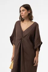 Vestido midi marrón de lino, con escote en V, mangas cortas amplias y detalle fruncido en el centro del frente. Presenta diseño asimétrico con dobladillo más largo en la parte trasera y corte relajado.