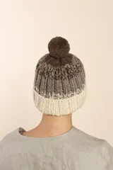 Gorro de punto degradé en tonos marrón y blanco, con diseño tejido en canalé y pompón superior claro.