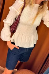 Camisa de color crudo con diseño fruncido tipo smock en el torso y mangas largas abullonadas con puños ajustados.