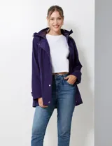 Gabardina impermeable de mujer, color morado oscuro, con capucha desmontable y cierre frontal oculto con botones a presión. Presenta bolsillos delanteros y ajuste interno en la cintura.
