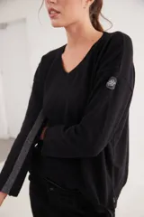 Buzo básico de escote en V y manga larga, confeccionado en lana. Presenta una raya lateral en contratono en una de las mangas y un pin de la marca aplicado en el hombro.