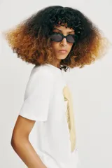 Camiseta de algodón con cuello redondo y manga corta. Presenta un diseño estampado frontal con efecto metalizado plateado sobre fondo rectangular.