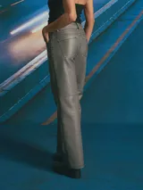 Pantalón de corte recto y tiro medio, confeccionado en material con acabado encerado color gris oscuro. Presenta costuras decorativas verticales a lo largo de las piernas y costura horizontal a la altura de la rodilla, con bolsillos laterales y cierre frontal.