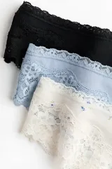 Pack de tres bombachas tipo Brazilian de tiro bajo, confeccionadas en punto de algodón y encaje. Incluye una de color negro liso, una celeste lisa y una de fondo crudo con estampado floreado pequeño. Todas cuentan con cintura en V con detalle de pequeño lazo en el centro y laterales de encaje.
