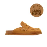 Zueco casual de cuero gamuzado color beige, con diseño tipo mocasín, costuras visibles y suela plana marrón.