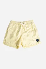 Short de baño liso color amarillo claro, con cintura elástica y cordón ajustable. Tiene dos bolsillos laterales, un bolsillo trasero y logo bordado.