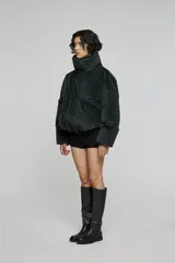Chaqueta acolchada de corte corto y volumen amplio, color verde oscuro. Presenta cuello alto envolvente, cierre frontal con cremallera oculta, bolsillos laterales integrados y mangas de línea amplia.
