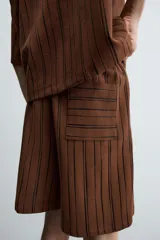 Bermuda de corte relajado color marrón con finas rayas verticales negras. Presenta cintura elástica ajustable con cordón y bolsillos laterales y trasero.