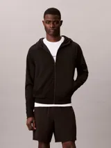 Buzo con capucha y cremallera Calvin Klein, de color negro, confeccionado en felpa de punto técnico y mezcla elástica ligera. Presenta cuello alto con capucha, cierre frontal de cremallera, bolsillos con cremallera en el pecho y la cintura, mangas largas con aberturas para el pulgar y detalle de bordado de la marca en el pecho.