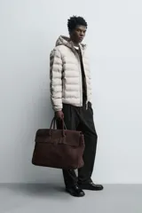 Campera puffer acolchada de corte regular fit en color negro, confeccionada en tejido técnico repelente al agua. Presenta cuello subido con capucha, cierre frontal de cremallera, mangas largas con puños elásticos y bolsillos laterales de vivo.