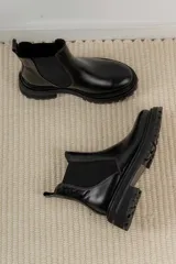 Bota Chelsea de cuero negro con elástico lateral y suela track.