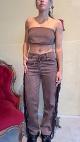 Pantalón marrón de gamuza con flecos laterales y ajuste con cordones en la cintura.