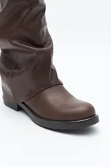 Bota de caña alta color negro, con diseño utilitario, puntera redondeada y taco bajo. Presenta un efecto fruncido en la caña y tres hebillas metálicas decorativas.