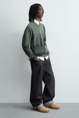 Bandolera negra con textura grabada, compartimento principal con cierre de cremallera, bolsillo interior con cremallera, bolsillo plano frontal, asa de hombro ajustable y extraíble.