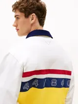 Chomba de rugby Tommy Hilfiger Sailing, unisex, de corte amplio y hombros caídos. Diseño color block blanco, amarillo y azul, con logo de la marca bordado en el pecho.