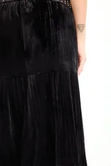 Falda larga de color negro con textura símil terciopelo, presenta un diseño con volados y detalle de tachas en la cintura.