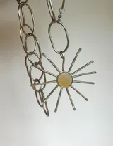 Collar con cadena de eslabones plateados y dije artesanal con forma de sol, con centro de nácar y rayos de alpaca.