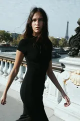 Vestido largo negro de cuello redondo y manga corta, con detalle de drapeado lateral, bajo con abertura lateral y cierre de cremallera en la espalda.