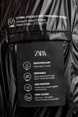 Campera puffer negra con capucha, cierre frontal con cremallera, bolsillos laterales con cremallera y puños elásticos.