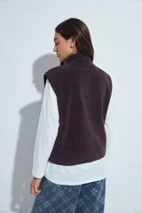 Chaleco de corderito color marrón oscuro, con cierre frontal completo, cuello alto y bolsillos laterales.