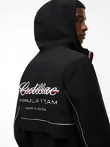 Cortavientos negro con capucha fija, cierre frontal de cremallera con cinta distintiva y puños elásticos. Presenta logos de la colaboración Cadillac Formula 1 Team en el pecho y diseño de corte regular.