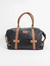 Bolso de viaje grande de cuero marrón con detalles en cuero negro, doble asa de mano y tiras decorativas verticales.