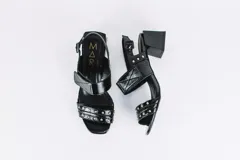 Sandalias negras de cuero charol con dos tiras, una sobre los dedos y otra sobre el empeine, ambas con apliques de tachas plateadas. Tira trasera con hebilla. Taco cuadrado.