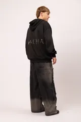 Pantalón de jean negro con proceso de lavado localizado y corte balloon fit. Presenta un diseño de recortes asimétricos, detalles de tachas metálicas y terminaciones desflecadas en el frente. Cuenta con bolsillos traseros clásicos y un calce holgado.